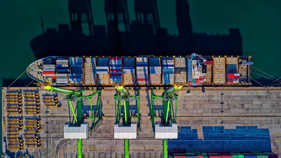 Aerial view of container ship at port being loaded by cranes