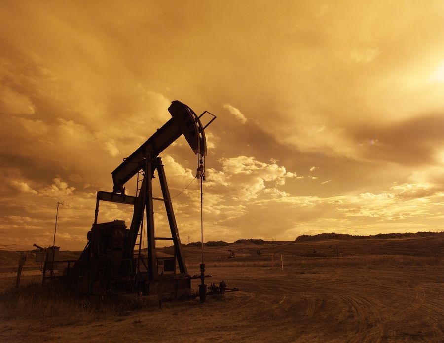 Oil pump jack silhouetted against a warm sunset sky